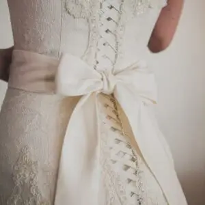 Preserve Your Wedding Dress blog | Sudsies Close-up of the back of an ivory lace wedding dress with corset lacing and a satin bow at the waist.