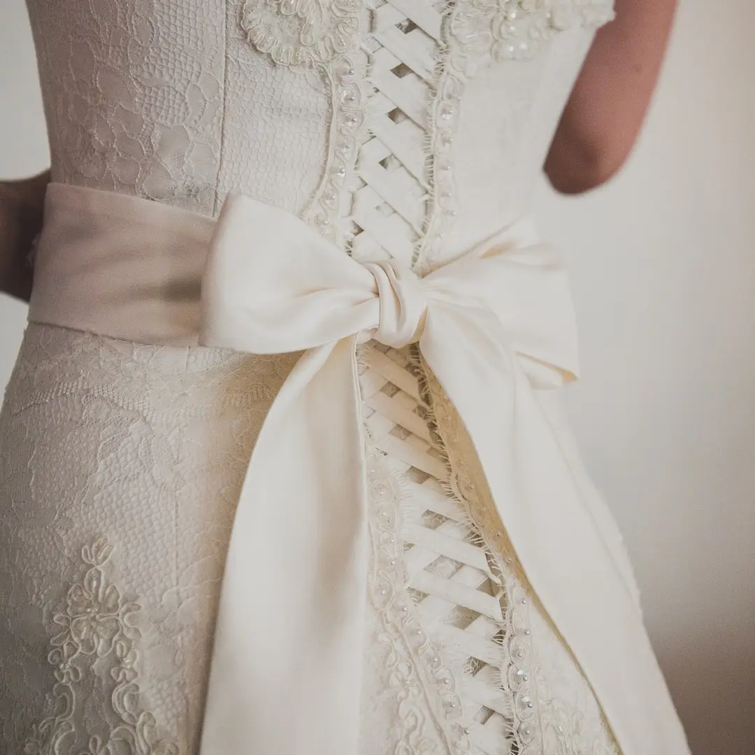 Close-up of the back of an ivory lace wedding dress with corset lacing and a satin bow at the waist.